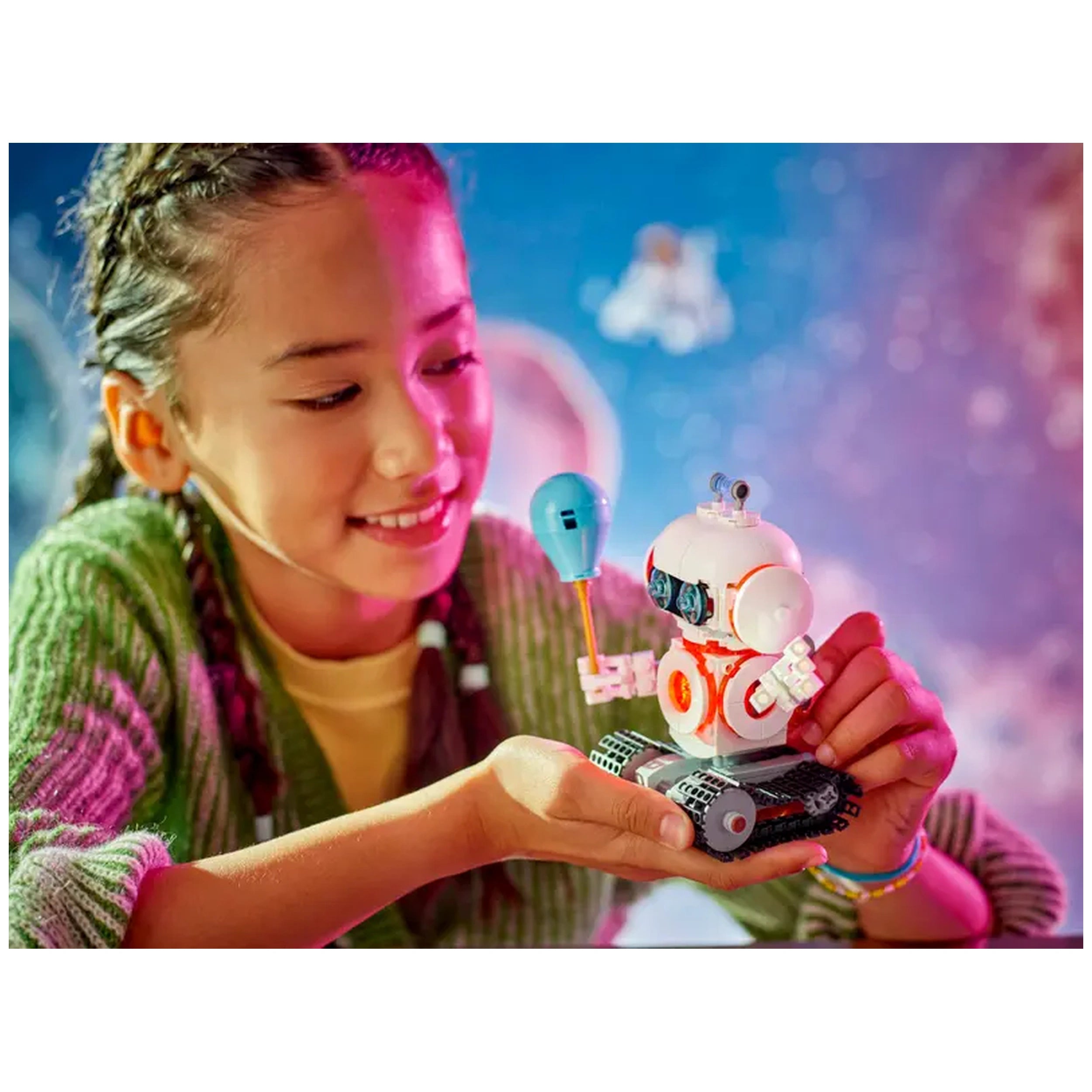 A child with braided hair smiles while holding a colorful LEGO® robot with a blue balloon. The robot features a white and orange design, moving tracks, and an expressive face, set against a vibrant, starry backdrop.