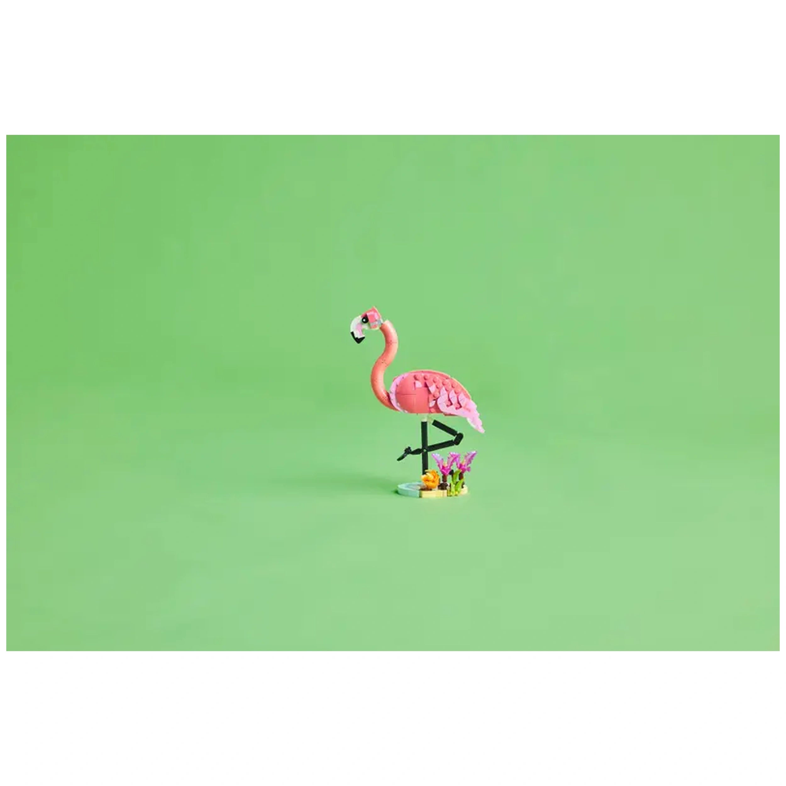 A vibrant pink LEGO flamingo stands on one leg, surrounded by colorful plant elements on a bright green background.