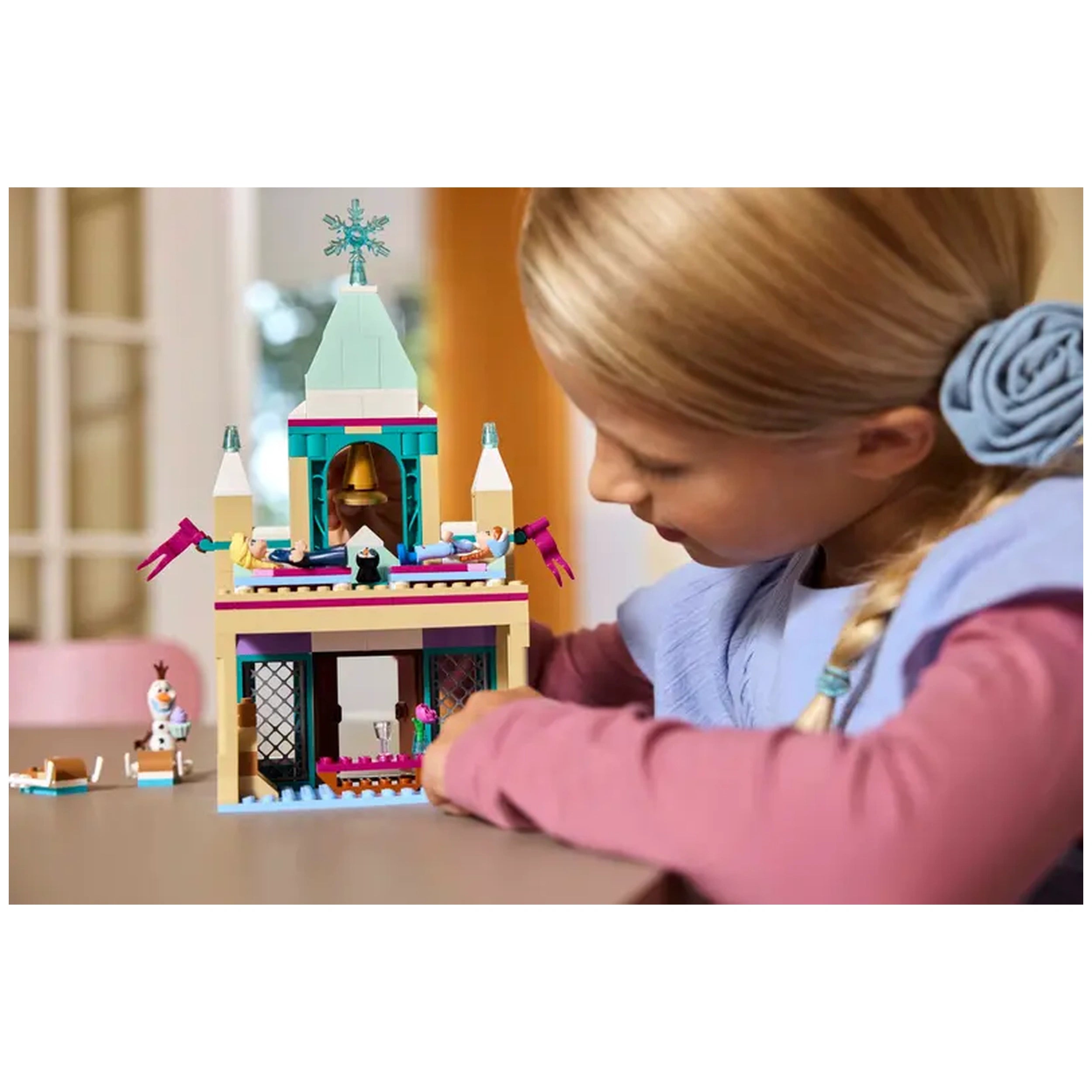 A young girl builds the intricate LEGO® Disney Frozen Arendelle Castle, featuring colorful towers and characters, including Olaf.