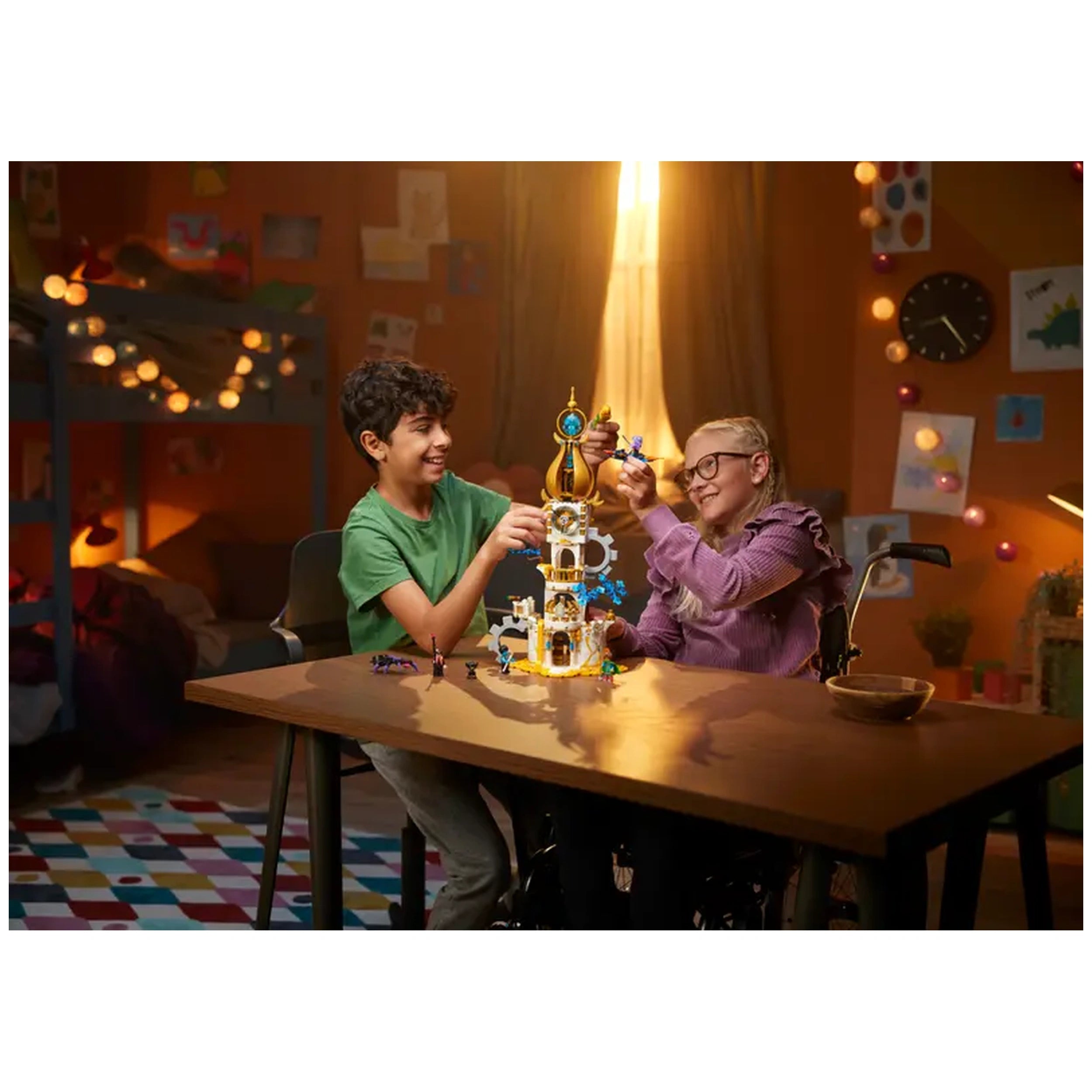 Two children, one in a green shirt and one in a purple top, joyfully build LEGO® DREAMZzz™ The Sandman's Tower on a wooden table in a cozy room. The tower features colorful decorations and a golden spire. The setting includes soft lighting, playful artwork on the walls, and a vibrant rug, creating a warm atmosphere perfect for imaginative play.