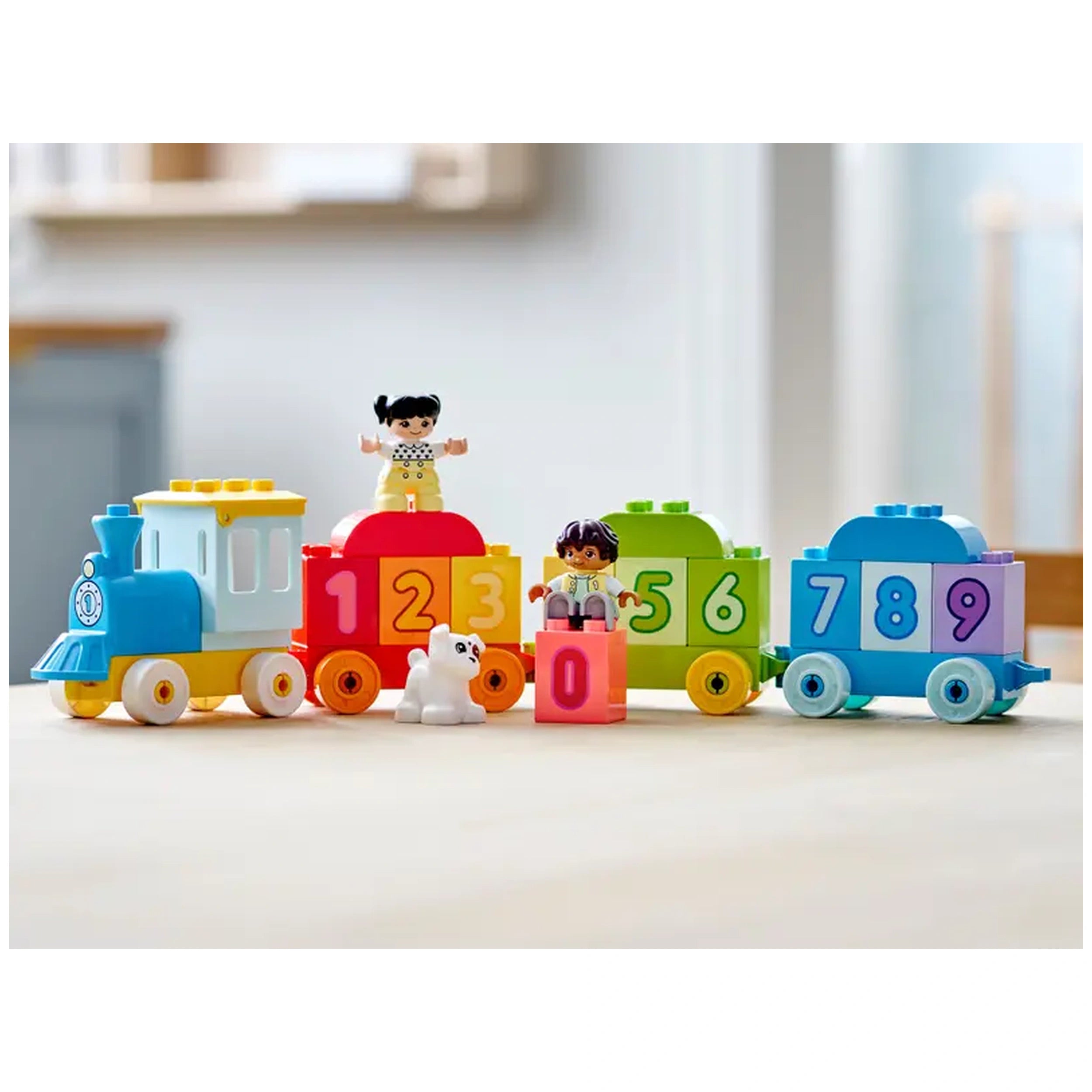 Colorful LEGO® DUPLO® Number Train set featuring a blue engine, vibrant numbered train cars, two figures, and a white dog, promoting counting play.