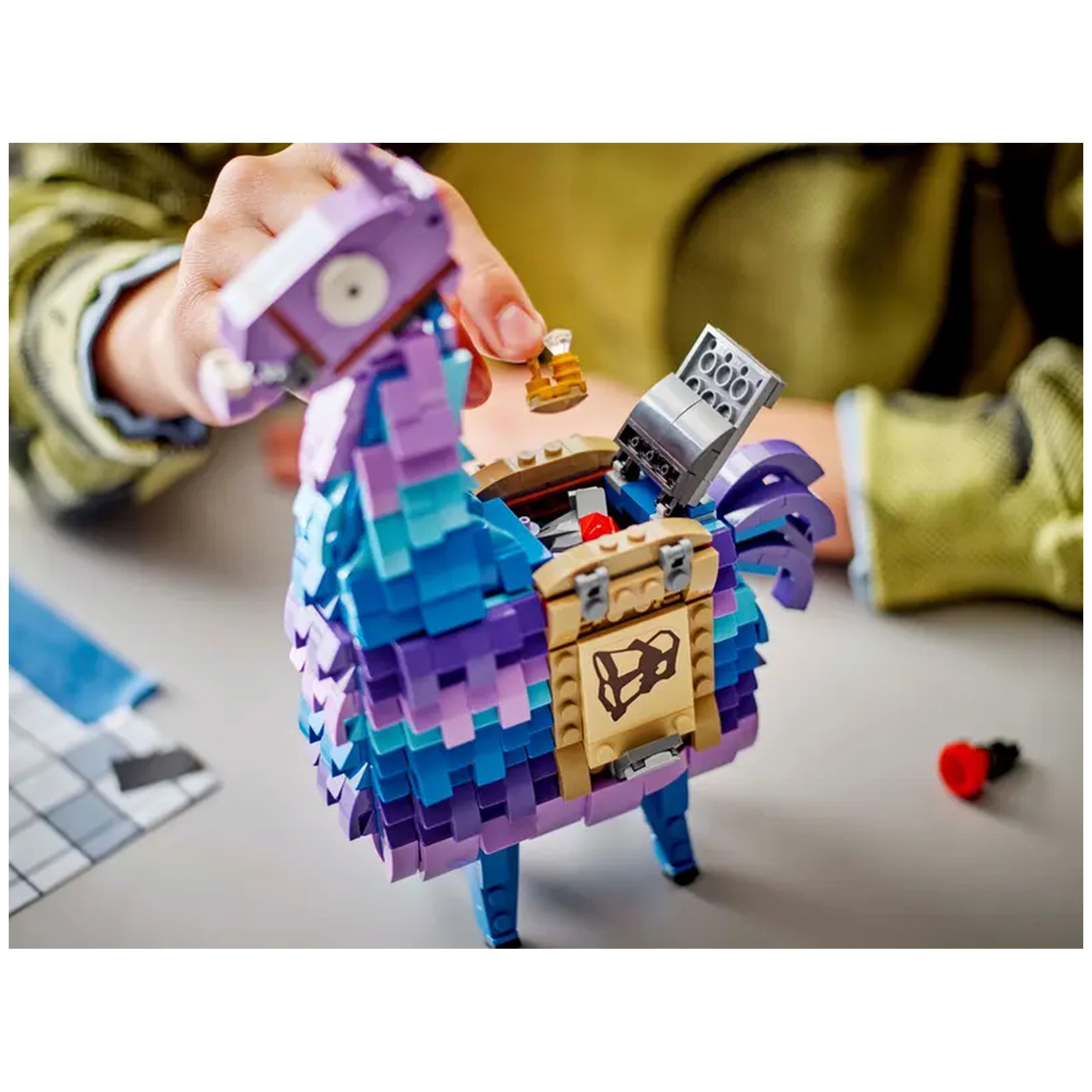 Colorful LEGO Fortnite Supply Llama construction set, with a child’s hand placing an accessory into its open mouth, revealing interior details.