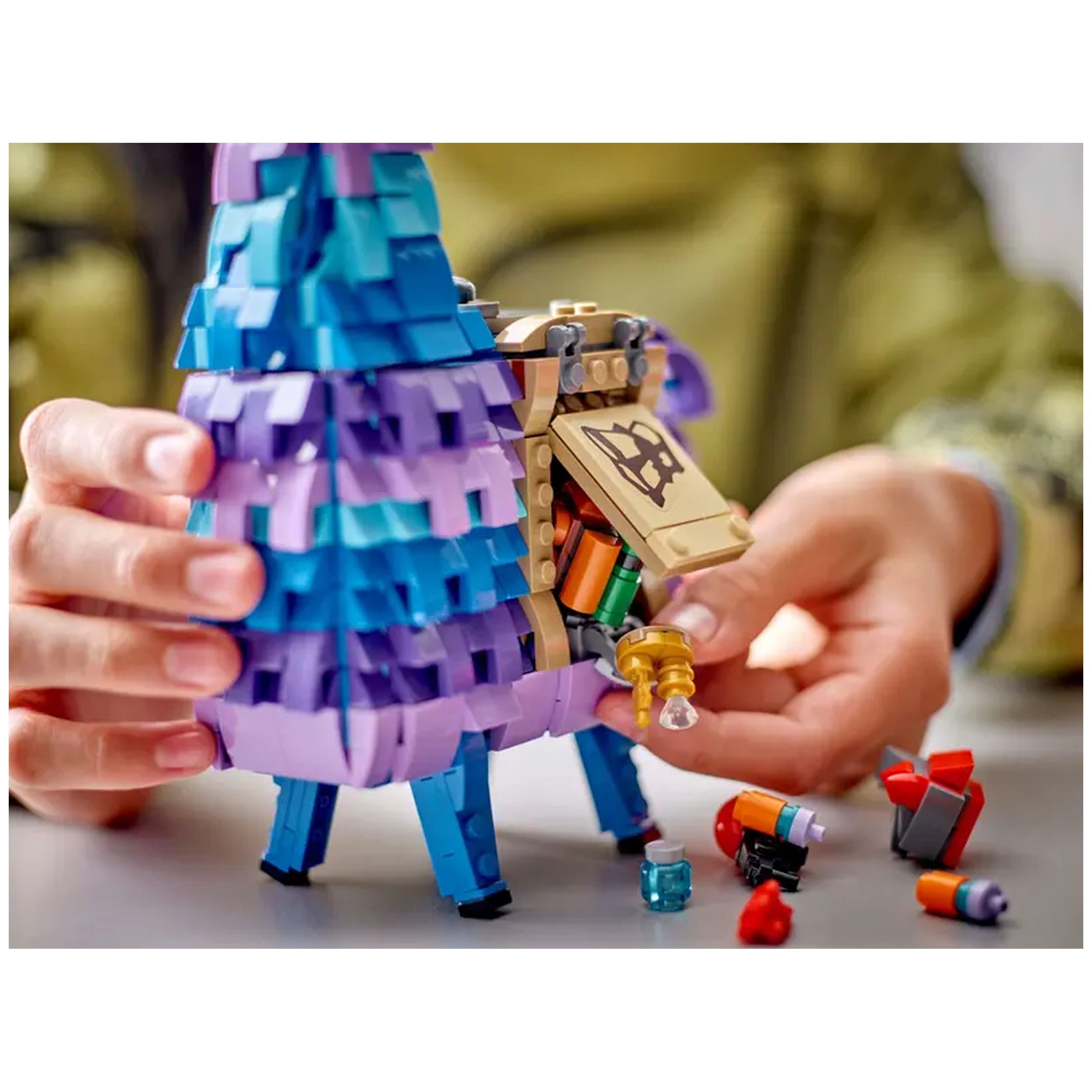 LEGO Fortnite Supply Llama construction set held in hands, featuring vibrant blue and purple details, with an opened side revealing colorful accessories scattered on the table.