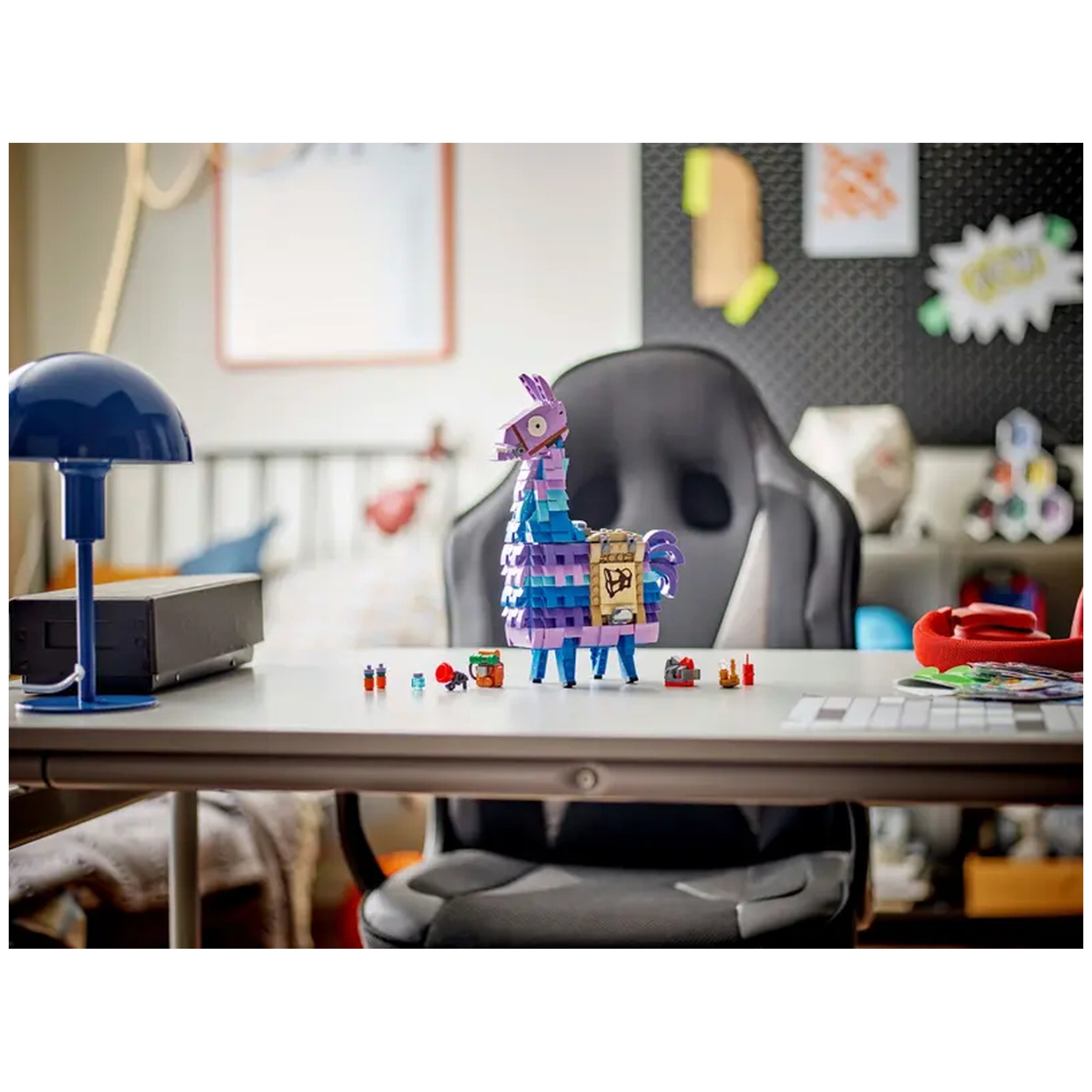 LEGO Fortnite Supply Llama construction set stands on a desk, surrounded by game-themed accessories, with a desk lamp in the foreground.