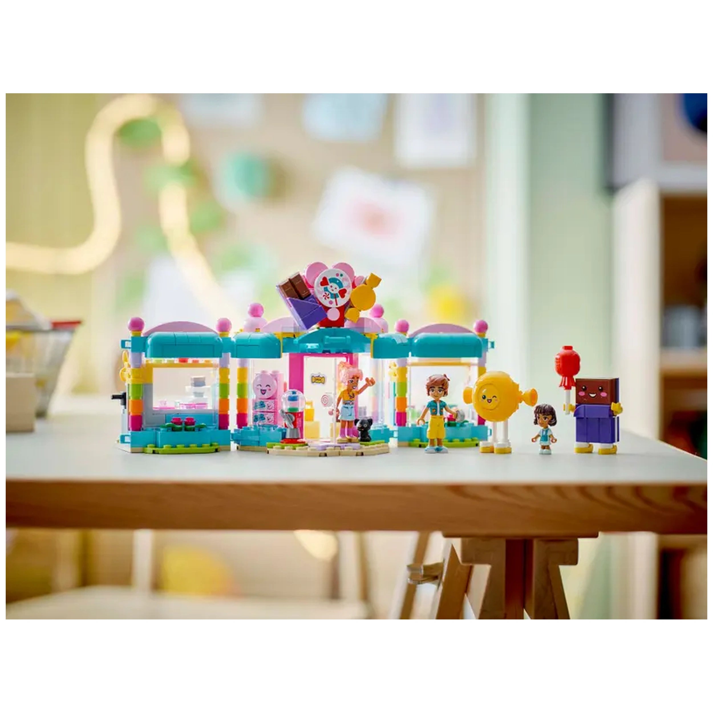 LEGO Friends Heartlake City Candy Store set featuring colorful buildings, mini-dolls, a playful cat figure, and candy-themed decorations on a wooden table.