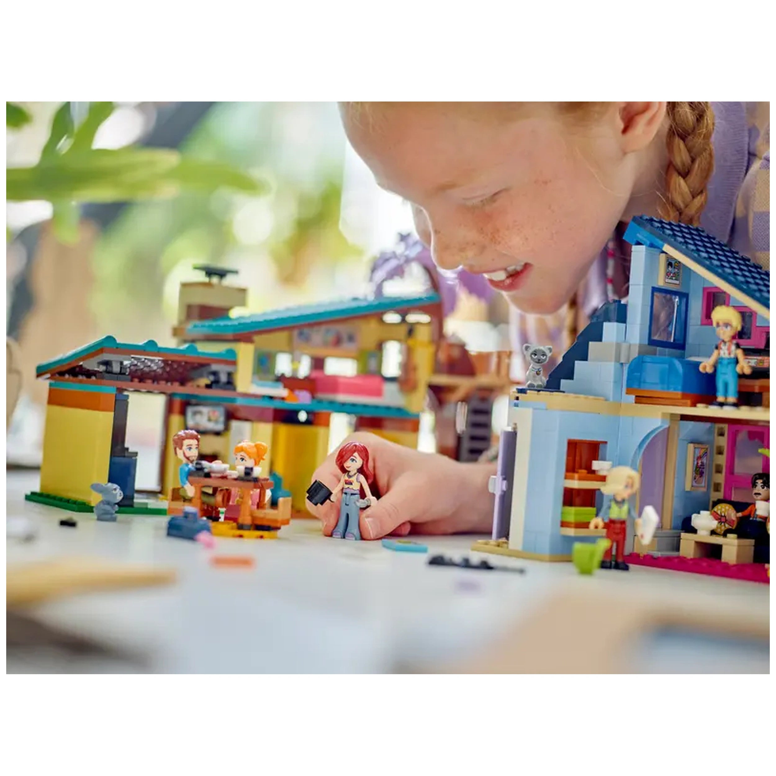 A child joyfully plays with the LEGO Friends Olly and Paisley's Family Houses set, featuring two colorful houses and mini-dolls.