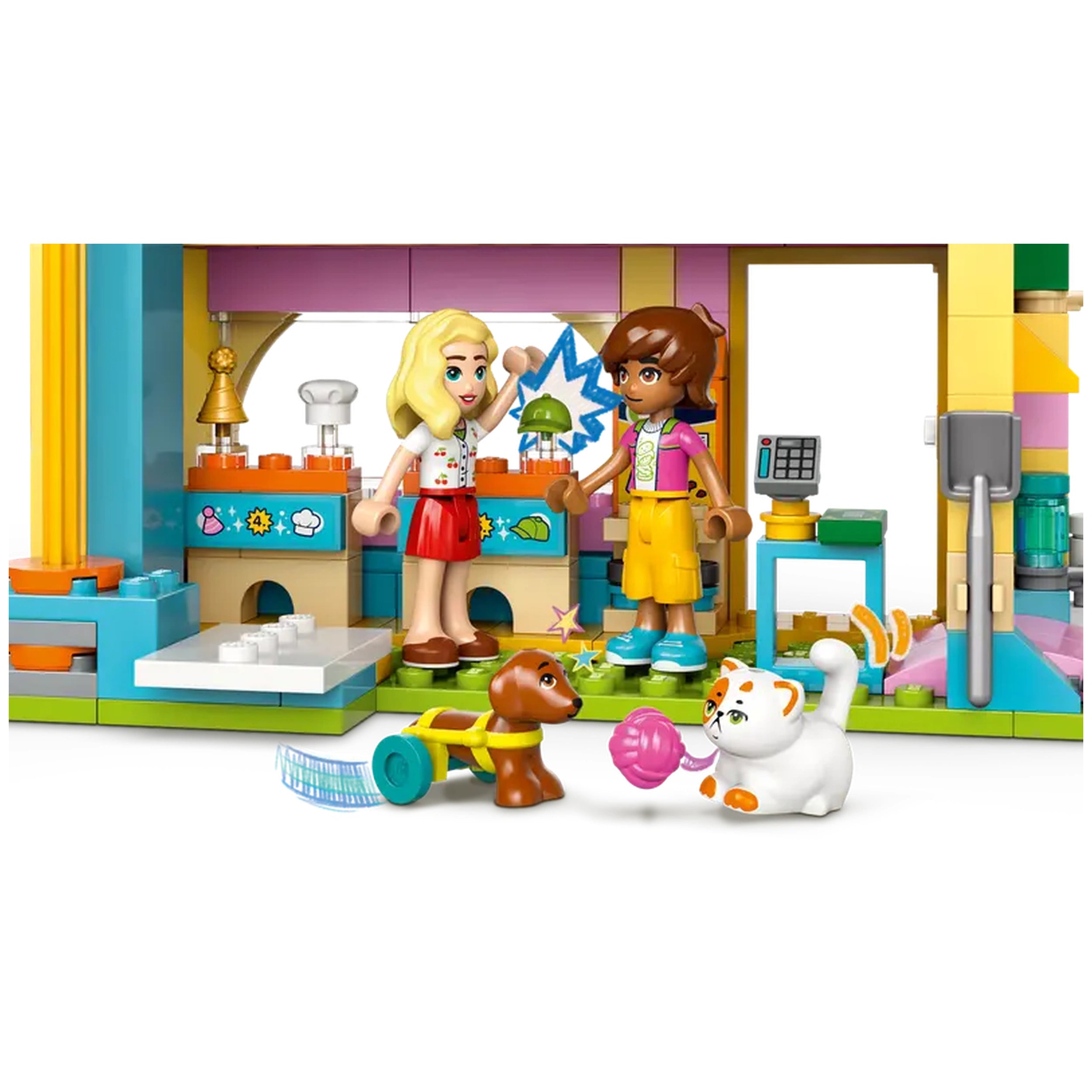 Two LEGO® Friends minidolls, one with blonde hair and a red skirt, the other with brown hair and colorful clothing, interact excitedly in a brightly colored pet accessories shop. A playful brown dog and a white cat with orange spots are on the floor, surrounded by pet toys and accessories. The shop features vibrant decor and a variety of pet care items, creating an engaging environment for imaginative play.