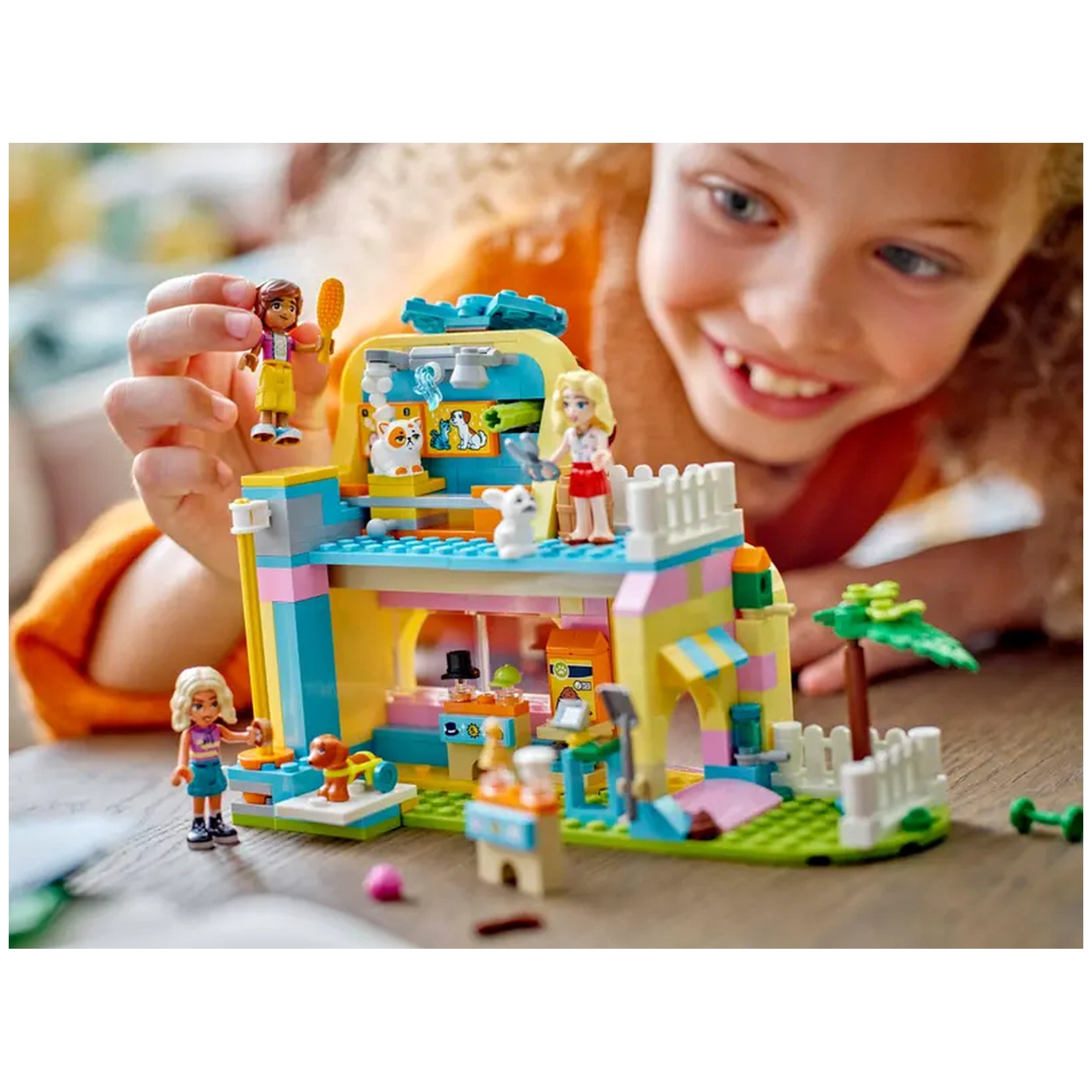 A smiling child plays with the colorful LEGO® Friends Pet Accessories Shop set, featuring minidolls and cute pet figures.