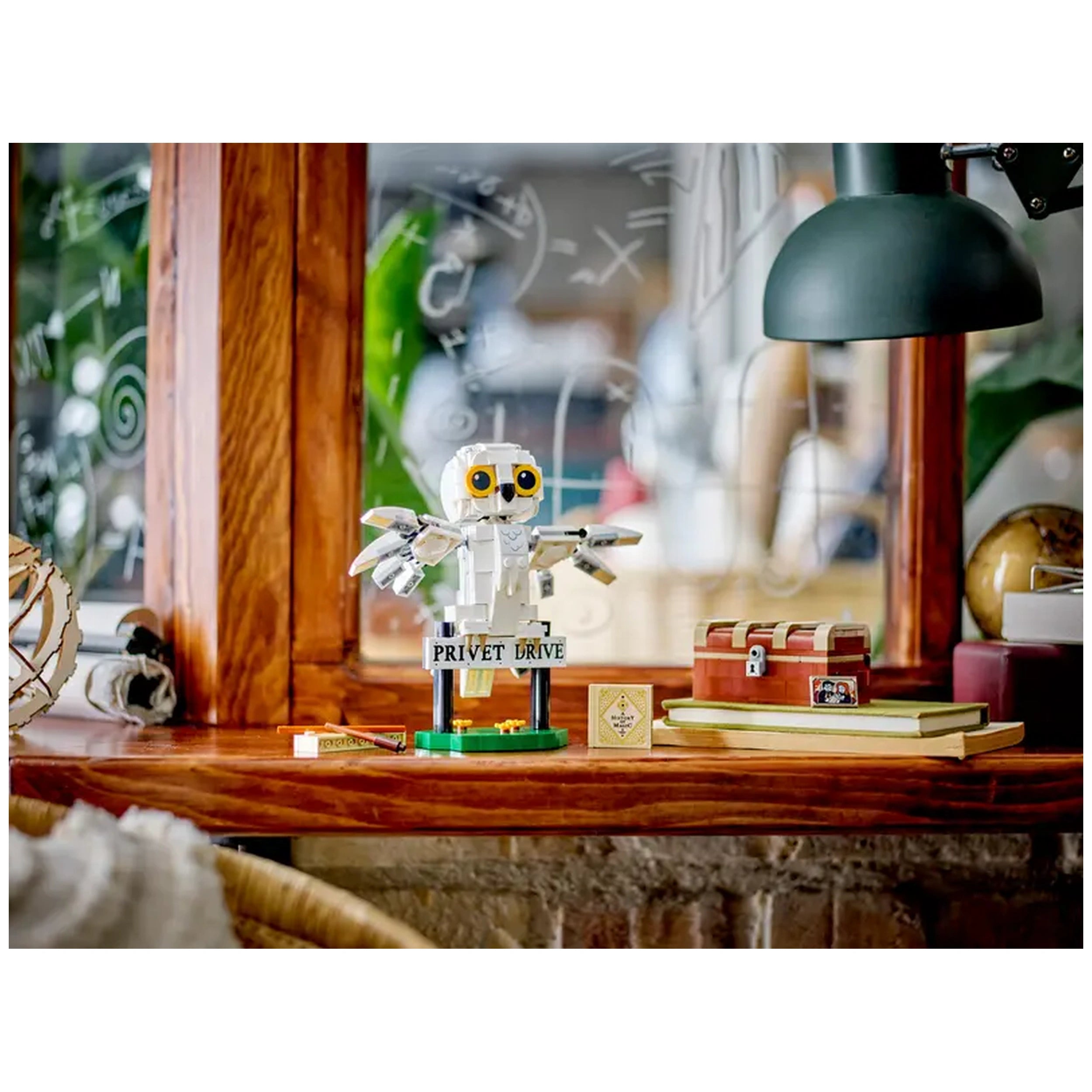 LEGO Harry Potter Hedwig figure stands on a 'Privet Drive' sign, surrounded by books and a treasure chest against a wooden shelf backdrop.