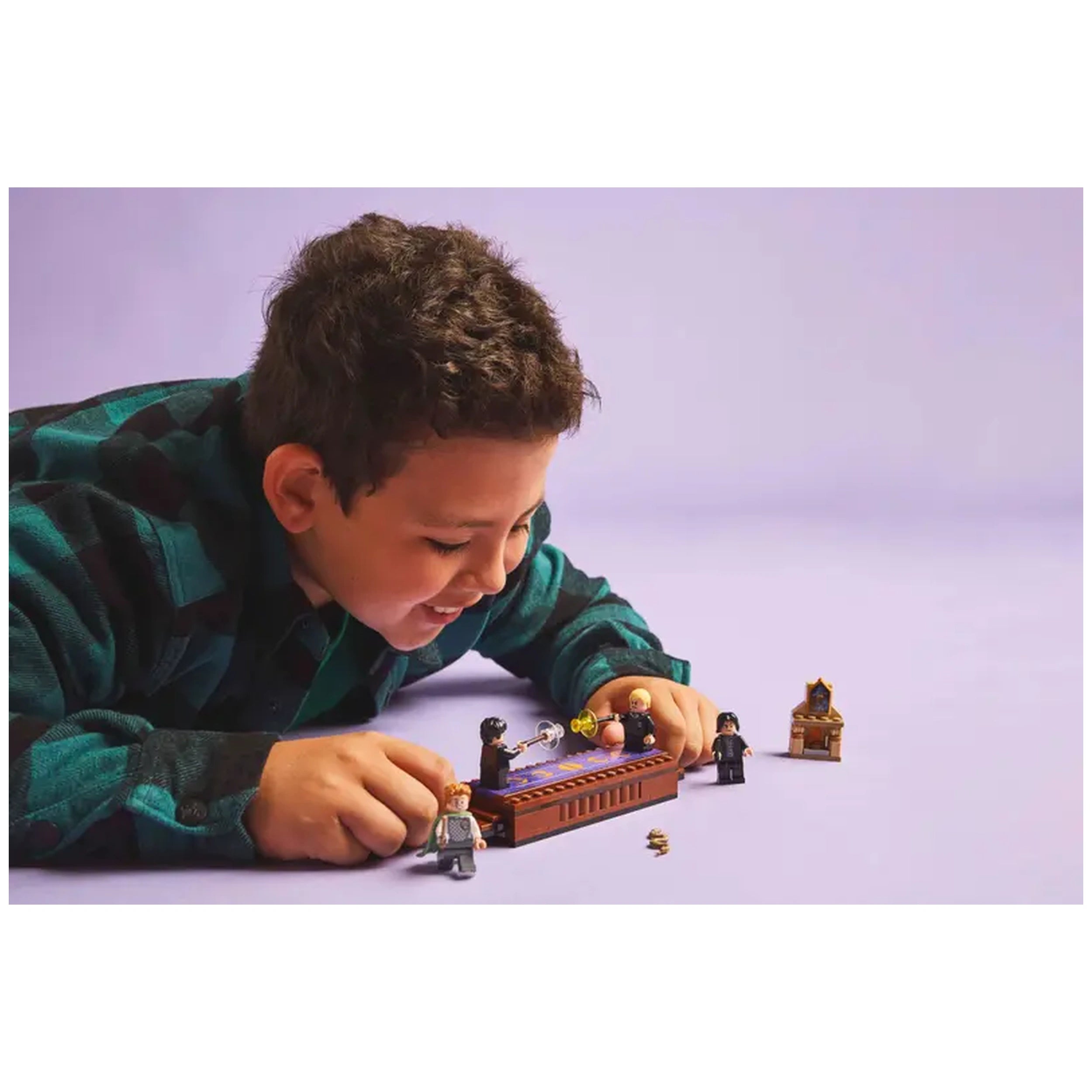 A child joyfully plays with the LEGO Harry Potter Dueling Club set, manipulating minifigures on a battle platform against a pastel purple background.