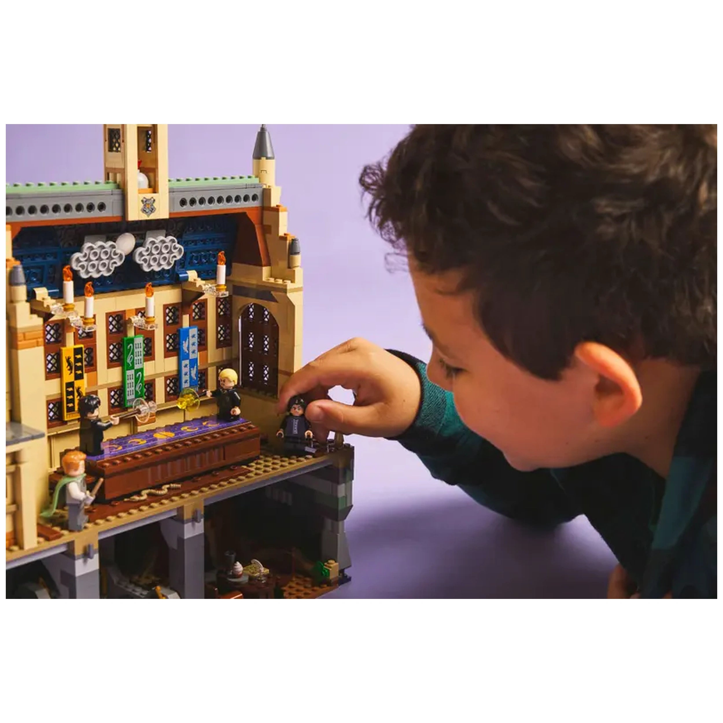 A child adjusts a minifigure on a detailed LEGO Hogwarts Castle Dueling Club set, featuring intricate decorations and vibrant colors.