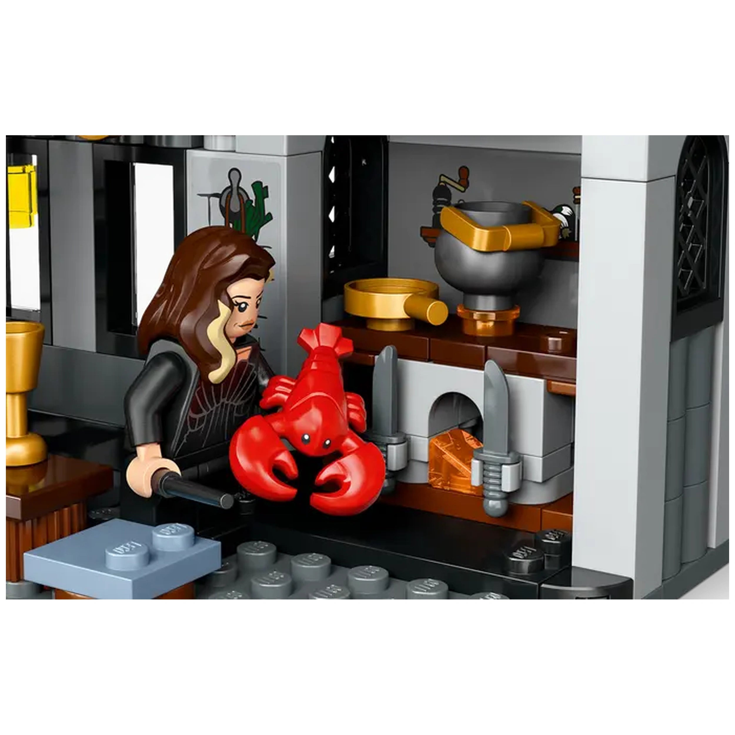 A LEGO® Harry Potter™ figure holds a red lobster in a detailed Malfoy Manor kitchen, featuring a fireplace, cauldron, and golden utensils.