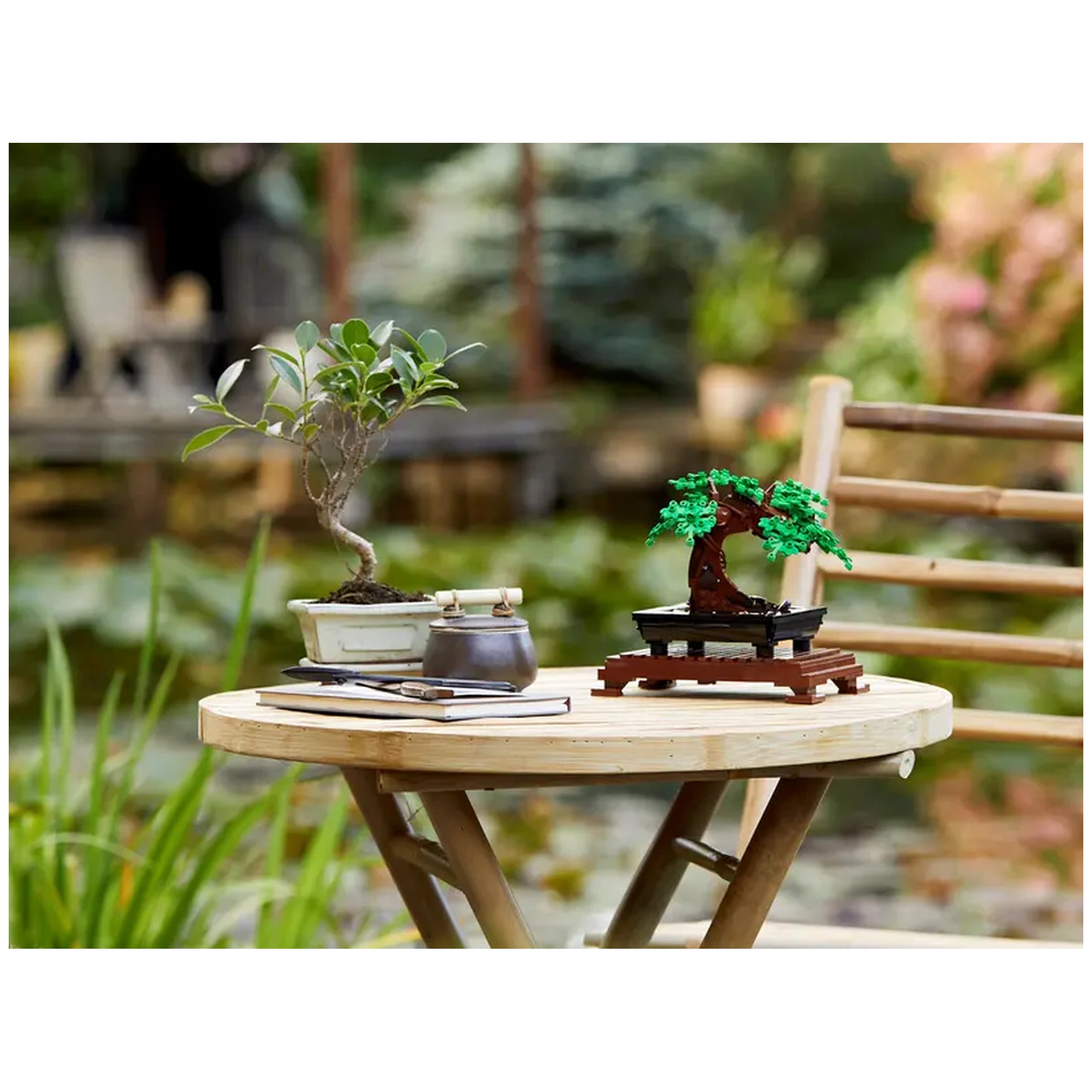 Lego Bonsai Tree model set on a wooden table beside a real bonsai plant, with green leaves and a serene garden backdrop.