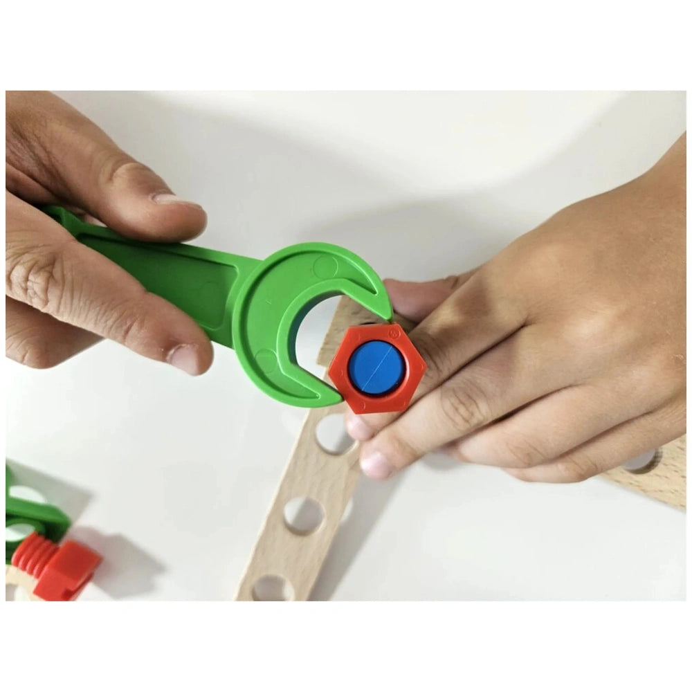 Child's hands assembling toy with a green wrench on a wooden plank using a red and blue screw from the Alexander Maly Constructor set.