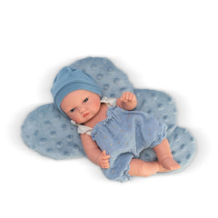 Bald doll in blue romper and hat, lying on a textured cloud-shaped cushion.