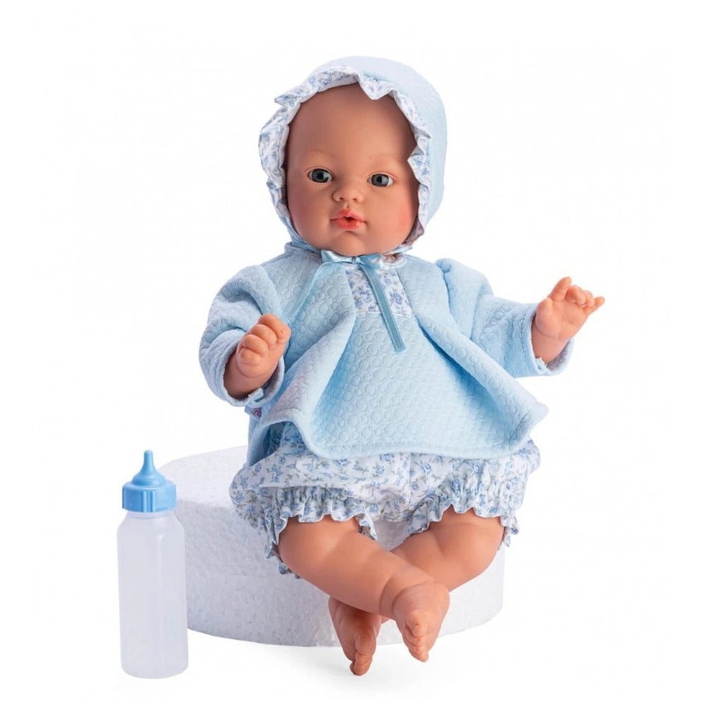 Soft-bodied doll with blue eyes and a bonnet, wearing a blue and flowered outfit, sitting next to a toy bottle.