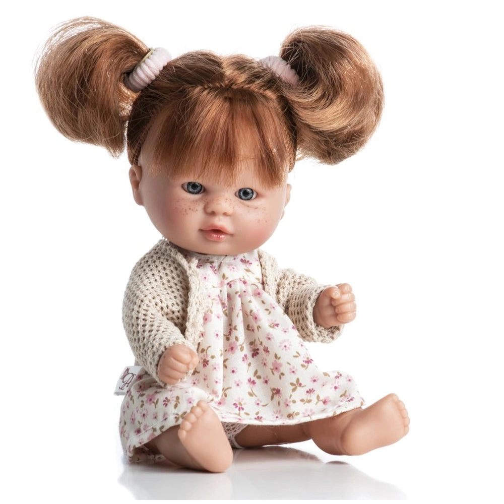 Laika doll with red pigtails, freckles, in a floral dress and knitted cardigan, sitting and smiling.