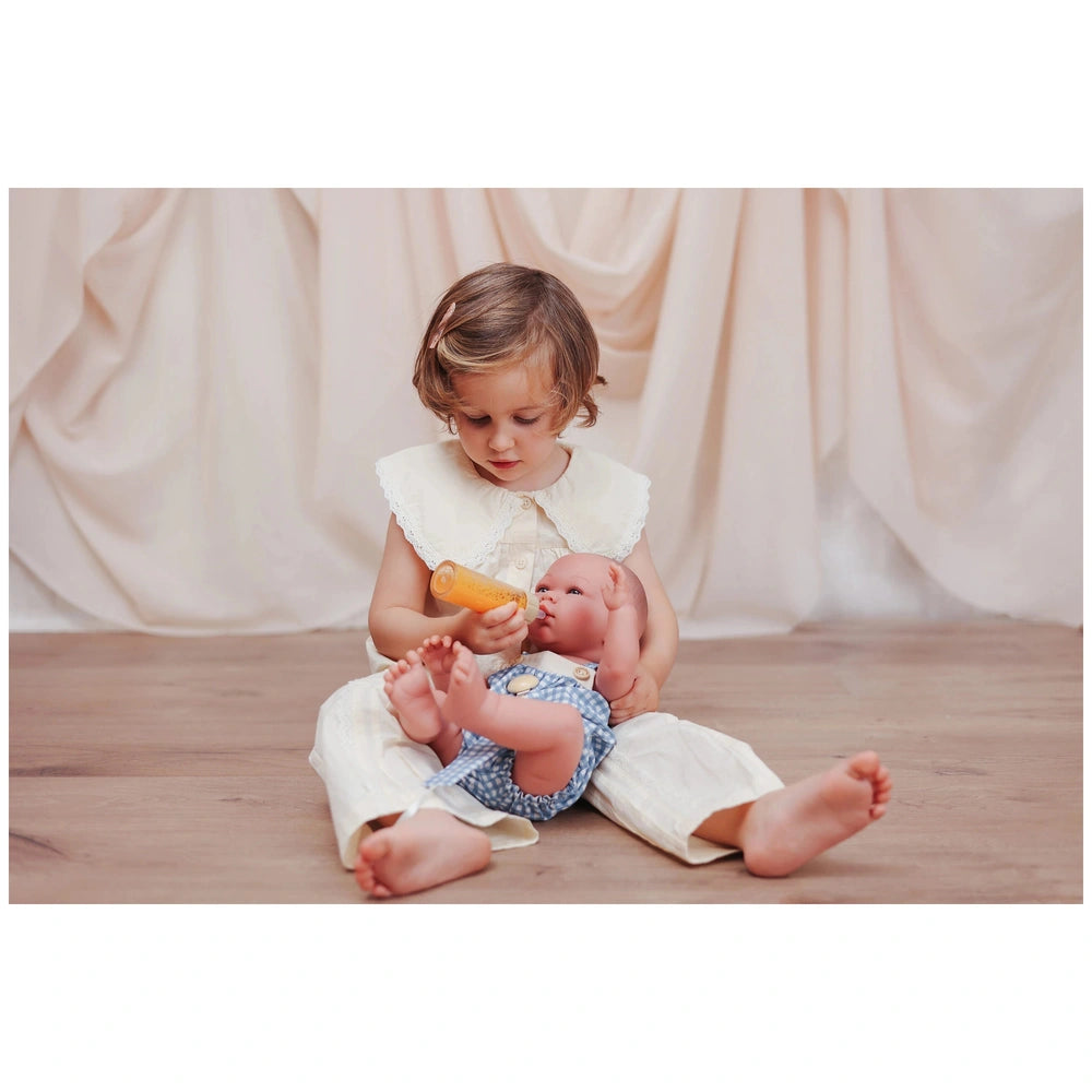ASI Dolls - Pablo and Maria Vinyl Dolls showcased with a child in a white dress, engaged with a small toy on a wooden floor.