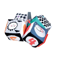 Baby Clementoni soft activity blocks in playful designs with varied colors, patterns, and face features, stacked casually.