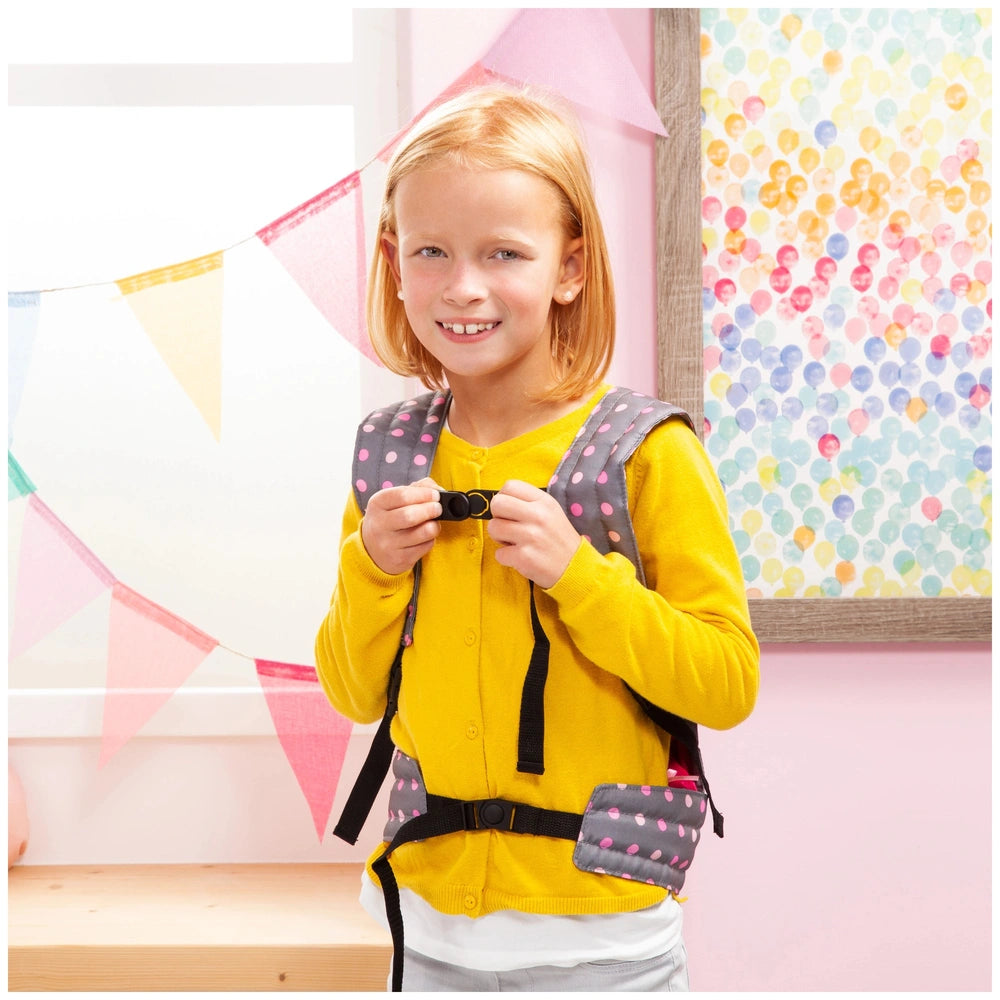 BAYER DESIGN Doll Carrier in gray and pink is held by a smiling girl in a yellow jacket against a colorful patterned backgrou