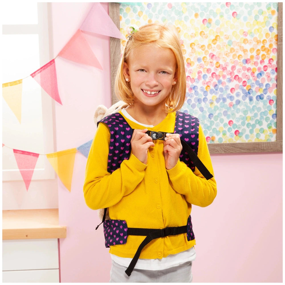 BAYER DESIGN doll carrier in unicorn blue and pink held by a smiling girl in a yellow sweater against a pink wall.