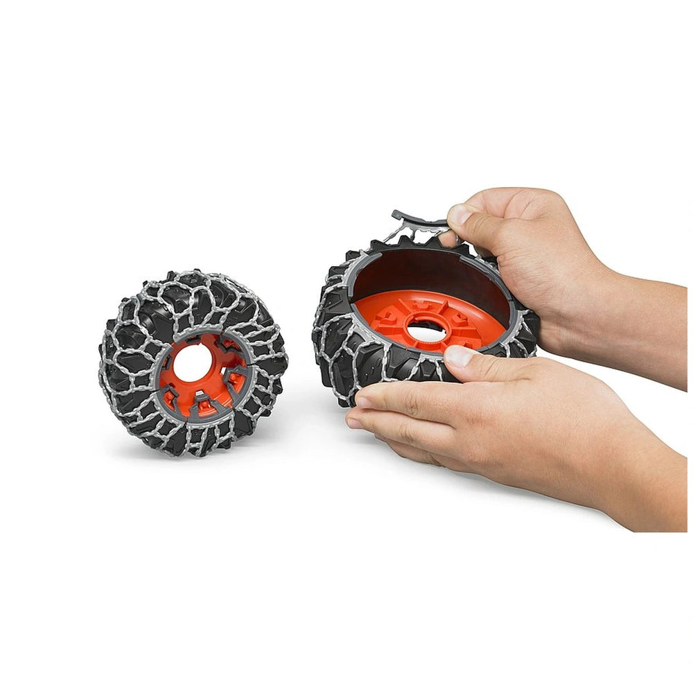 Hands assembling orange and gray snow chains on Bruder toy tractor wheels.