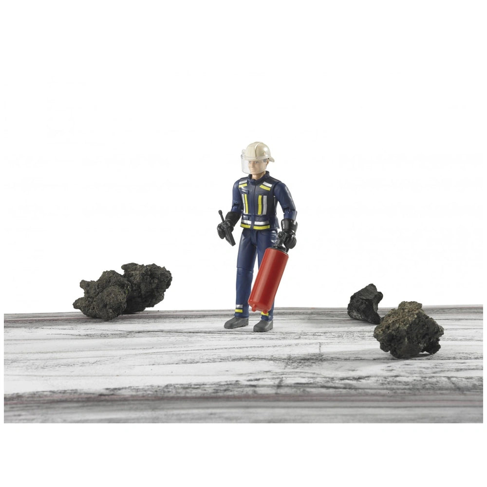 Bruder fireman figure in blue uniform with helmet, holding a red extinguisher, surrounded by rocks.