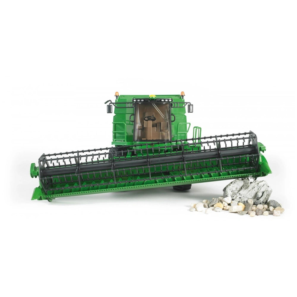 Green John Deere T670i combine harvester toy with detailed features on white background, rocks in front.