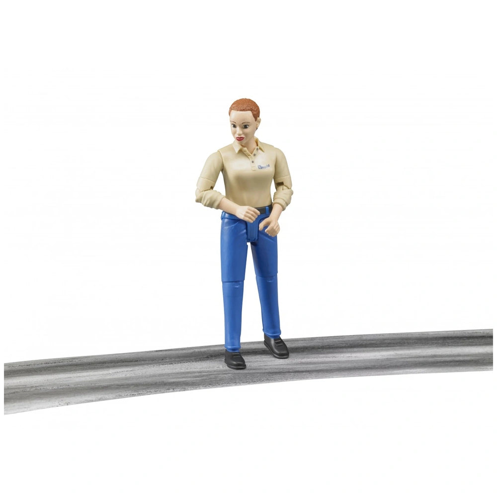 Bruder action figure with light skin, beige shirt, and blue trousers stands on a gray surface.