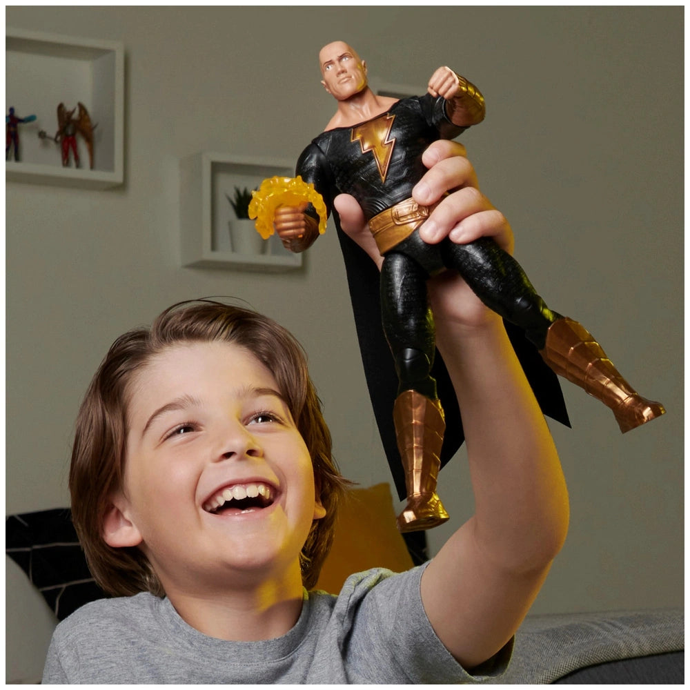 Young boy in a gray t-shirt smiles while holding a glossy Black Adam action figure with a black costume and gold accents.