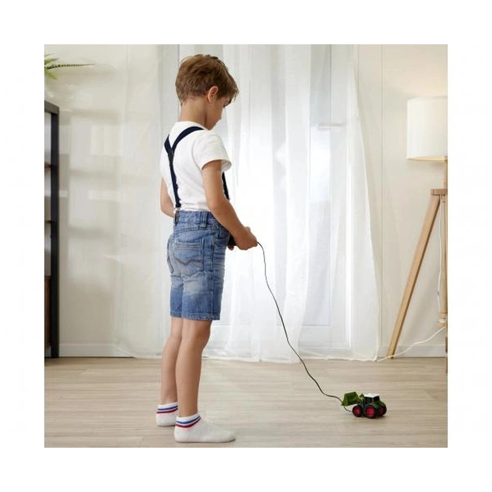 Dickie Fendt Remote Controlled Tractor play vehicle is operated by a child in a bright room with wooden floor and green plant