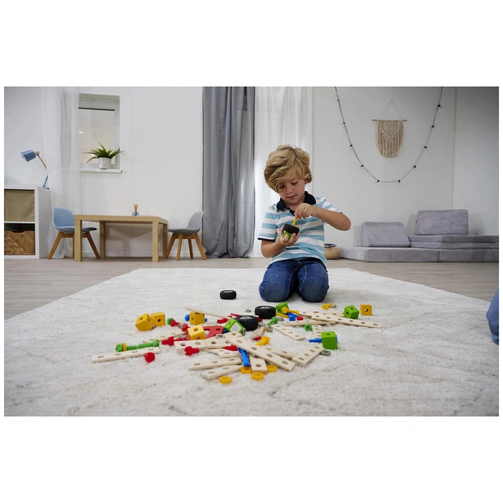 Eichhorn construction set toys are scattered around a young boy with blonde hair, engaged in play on a white shag rug.