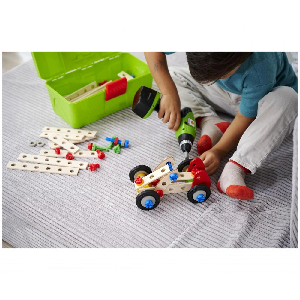 Eichhorn Constructor Racer Car set with a child using a green power drill to assemble the wooden toy car on the floor.