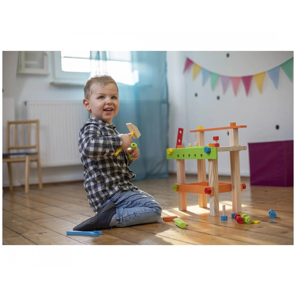 Eichhorn Work Bench showing a child playing with wooden blocks and a hammer in a bright, colorful indoor setting.
