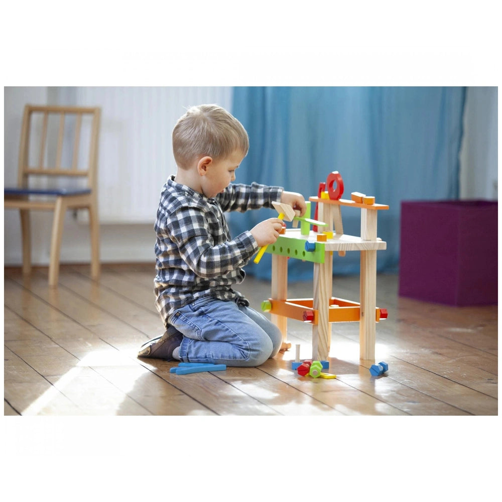 Eichhorn Work Bench shows a child in plaid shirt and jeans playing with a wooden construction toy in a cozy indoor setting.