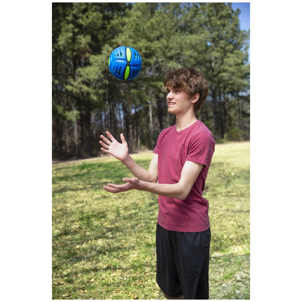 Goliath Wahu Phlat Ball Classic Sports Toy in the air above a person in a red t-shirt and black shorts on grass.