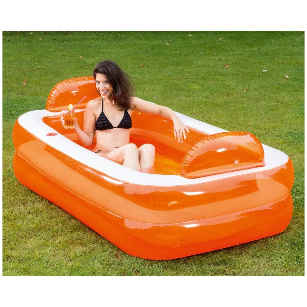 Woman in a black bikini relaxes in an orange inflatable pool with a white inner lining on green grass.