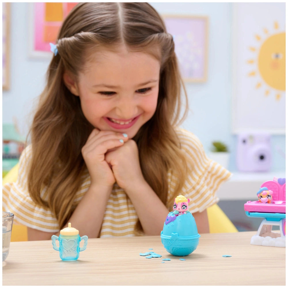 Hatchimals Alive playset with a blue egg-shaped toy and a pink toy is on the table in front of a smiling young girl.