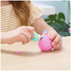 Hatchimals Alive playset featuring a pink and blue toy character held by a person at a wooden table with a plant in the backg