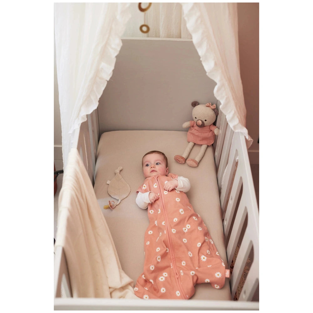 Jollein pacifier cloth with a baby in a pink floral outfit next to a white teddy bear on a beige bed with a canopy.
