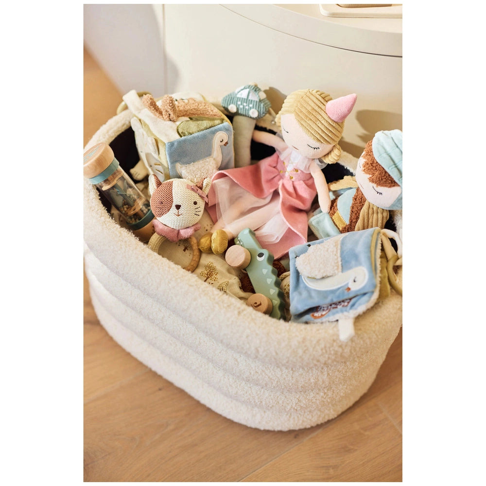 Jollein soft activity book in a white basket on light wood floor, filled with pastel plush toys in pink, blue, and white.