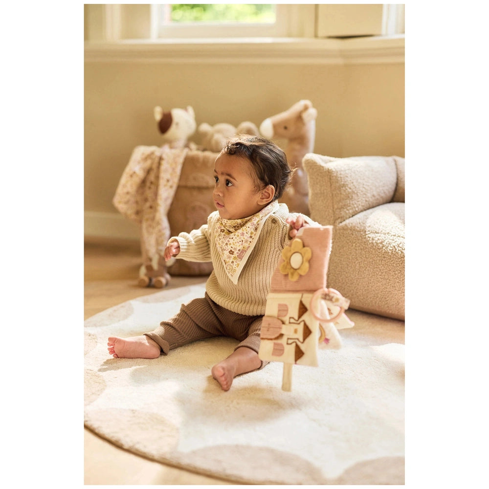Jollein Soft Activity Book featuring a baby in a beige sweater and brown pants, sitting on a beige rug, holding toys.