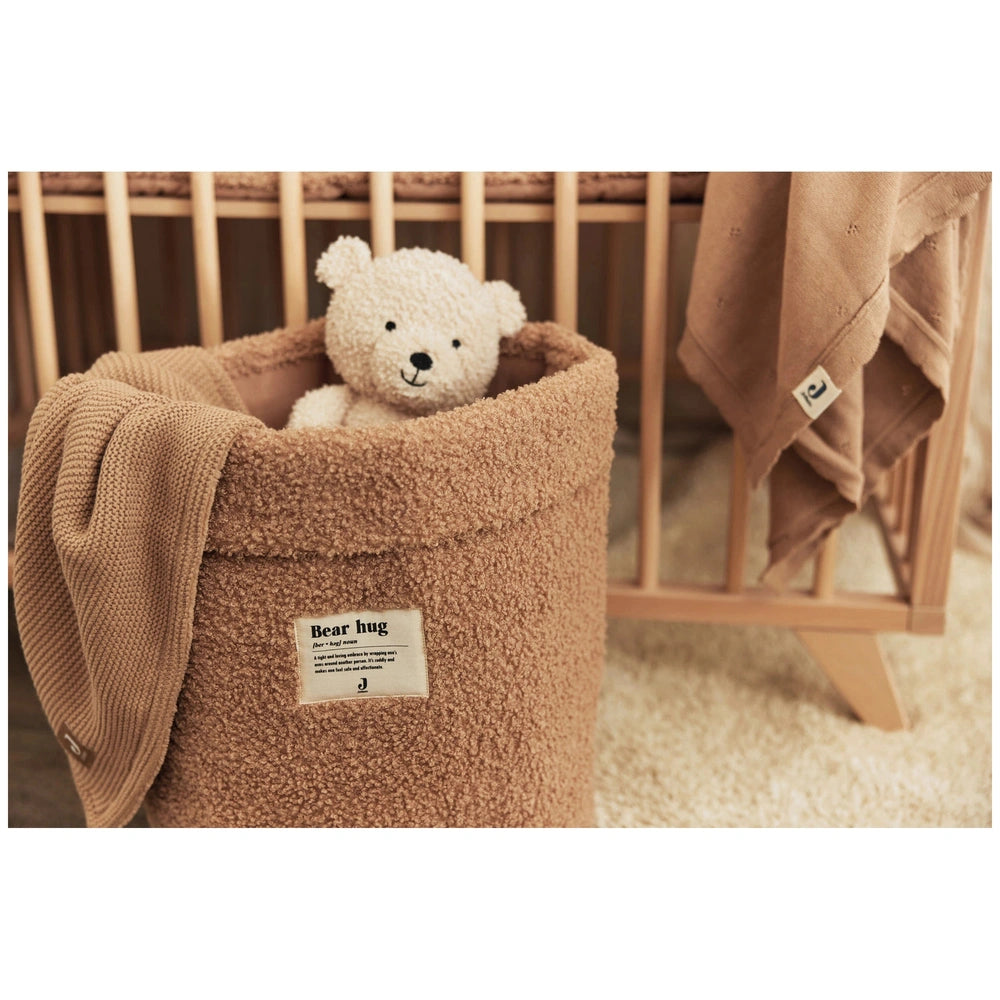 Jollein teddy bear plush toy on a beige blanket in a wooden crib with "Bear hug" text visible.