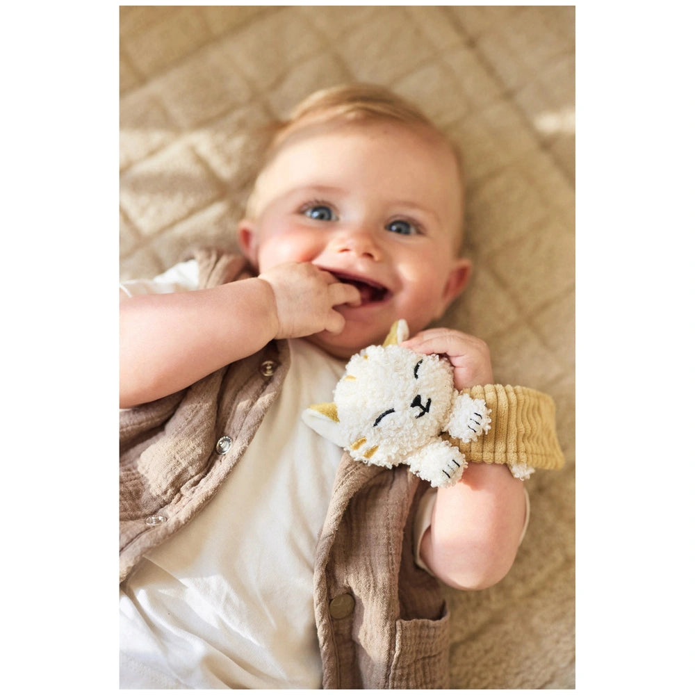 Jollein Wrist Rattle Tiny Park Charlie Cat Rattle held by a baby in a brown vest, featuring a white stuffed animal with black