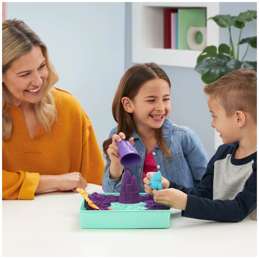 Kinetic Sand Sandbox Set is enjoyed by a smiling woman and two children in a bright playroom, engaging with colorful toys.