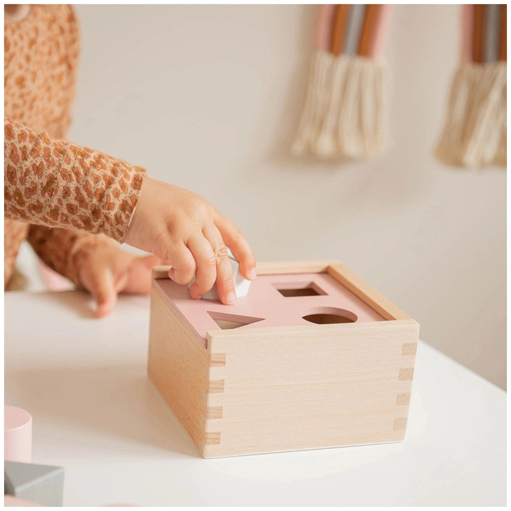 Wooden shape-sorting box with visible grain and pink interior, placed on a white surface.
