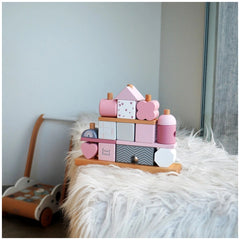Label-Label stacking blocks house in pink and white on a fluffy surface with a wooden toy car nearby.