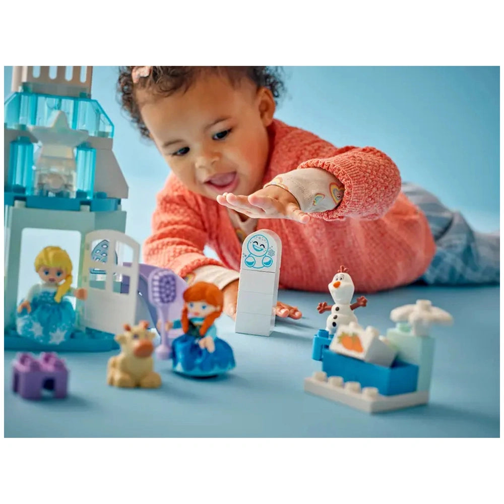 LEGO Anna and Elsa's Frozen Castle Party set is being reached for by a smiling child in a pink sweater on a blue surface.