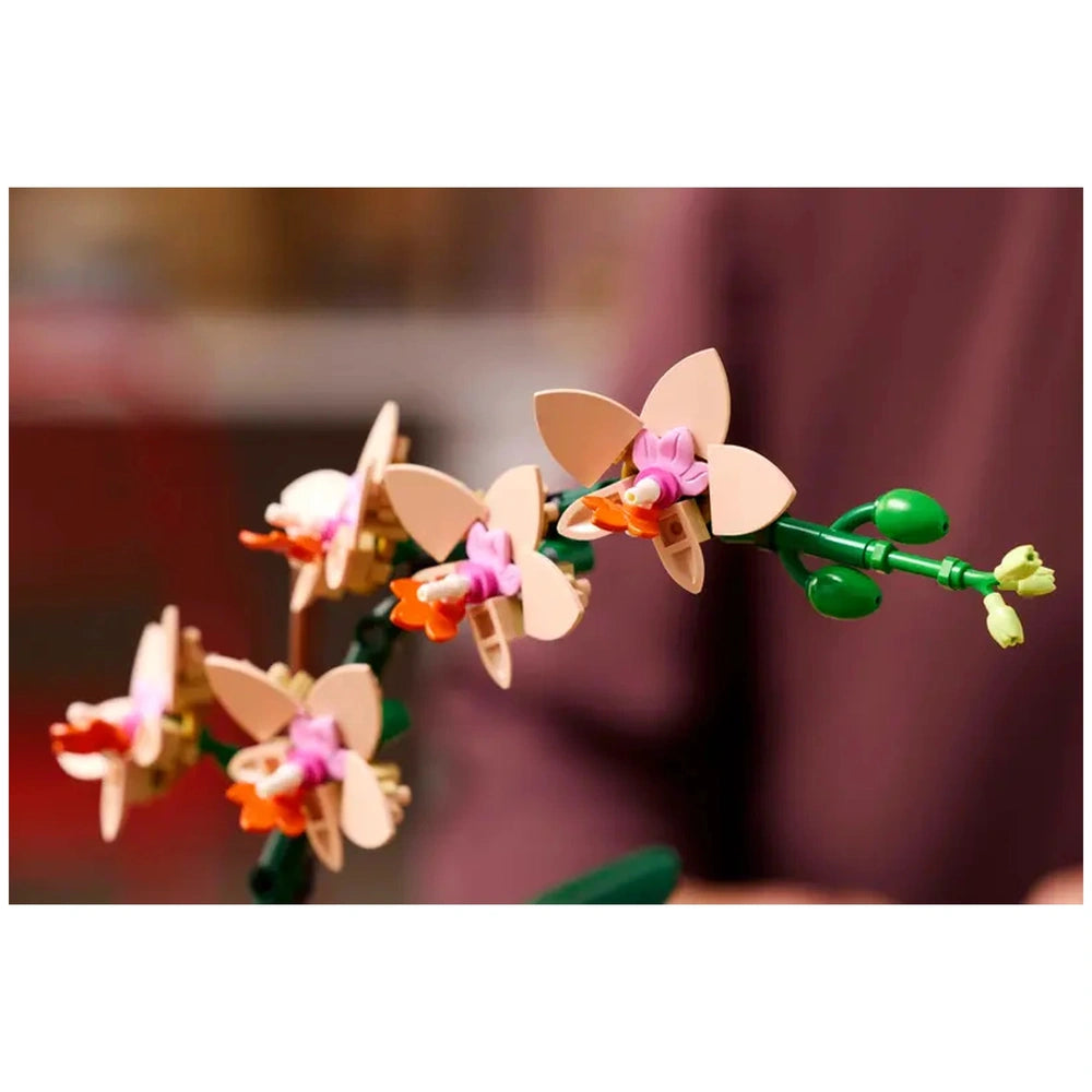 Delicate LEGO Botanicals Mini Orchid with five peach blooms, pink accents, and green leaves, showcasing intricate details against a blurred background.