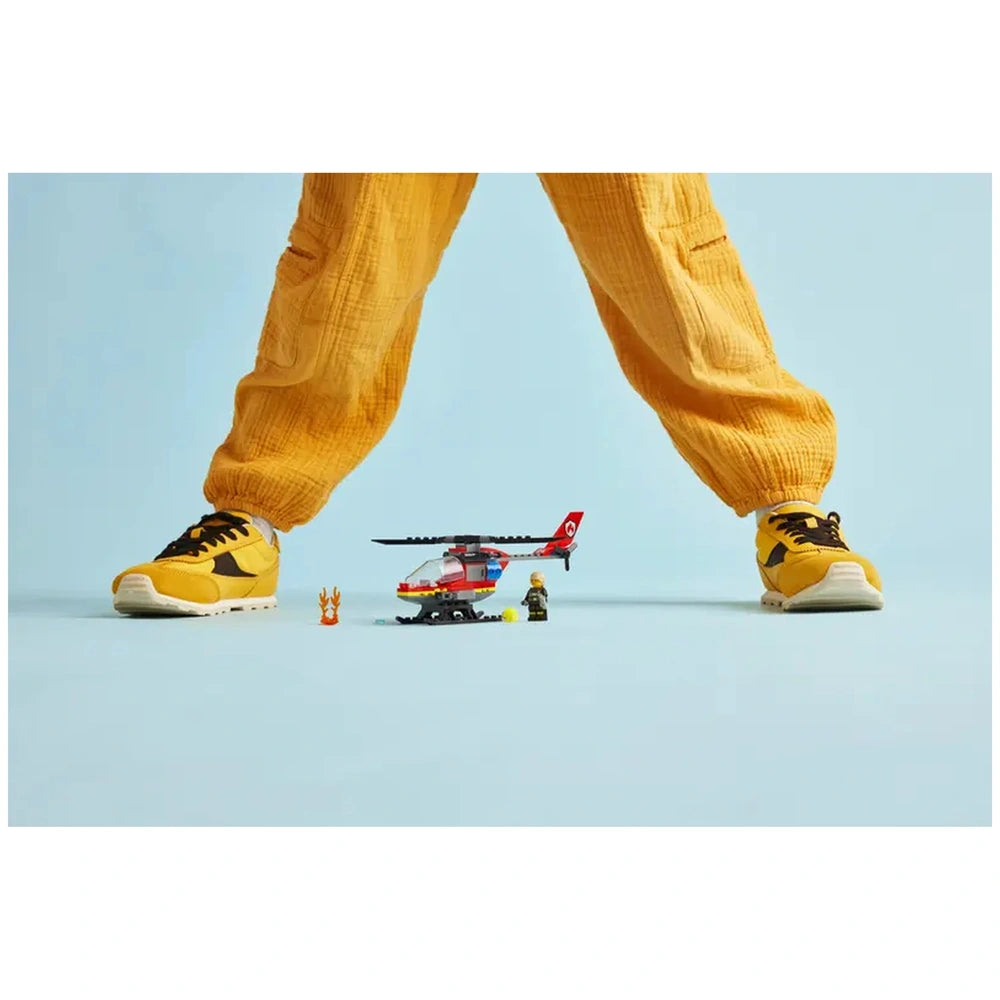 Lego City Fire Rescue Helicopter set with minifigures on the ground, framed by a child's yellow pants and sneakers.
